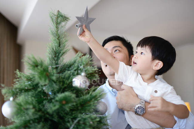 Счастливый молодой азиатский отец и сын украшая елку — стоковое фото