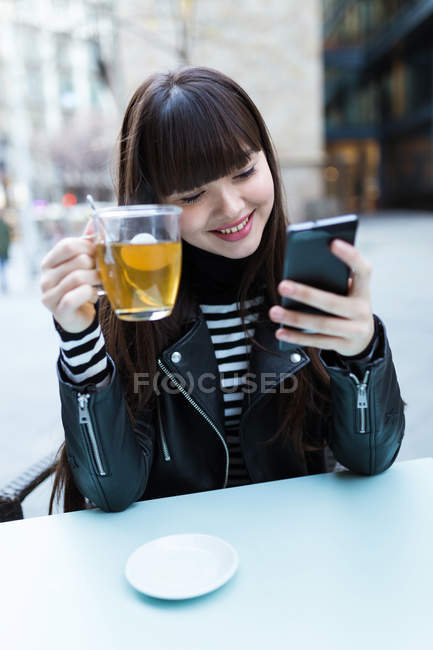 Young attractive asian woman in city using smartphone and having tea — Stock Photo