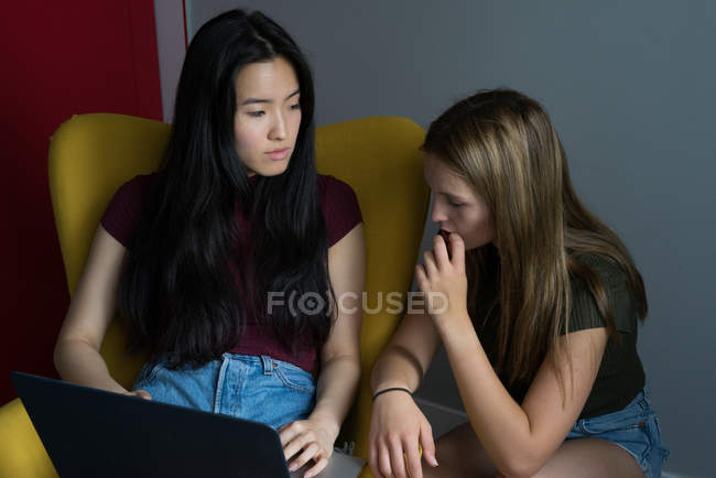 Chinese woman with a friend and laptop having fun in a yellow armchair. — Stock Photo