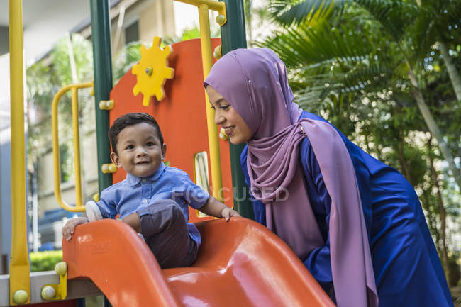 Joven asiático musulmán madre y niño jugando en parque infantil - foto de stock