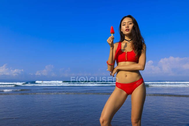 Chica asiática en una playa en bikini con un helado en la mano . - foto de stock