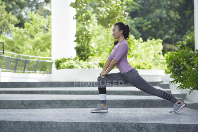 Eine junge asiatische Frau dehnt sich vor ihrem täglichen Lauftraining in Singapores City. — Stockfoto