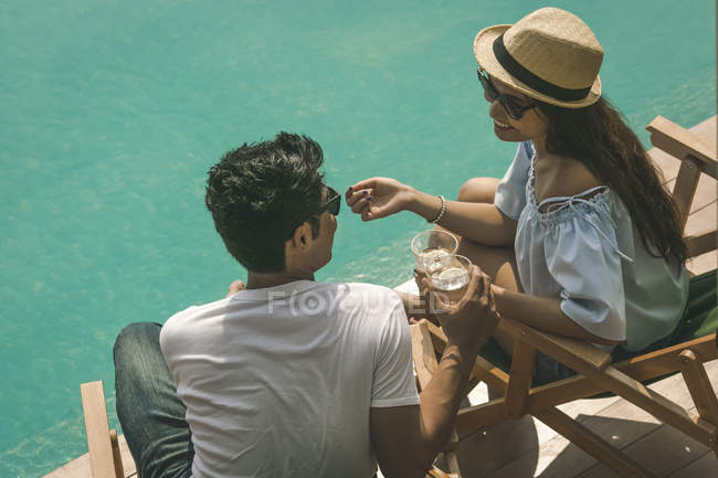 Jovem casal relaxante com bebida perto da piscina — Fotografia de Stock
