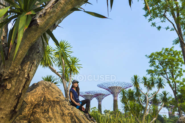Молода жінка сінгапурських відпочиває в саду біля затоки від неї тренування. Пляшку води знаходиться поруч з нею. — стокове фото