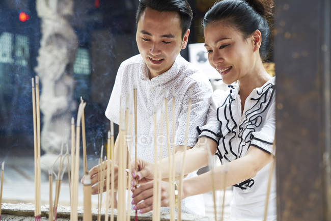 Giovane asiatico uomo e donna pregando nel tempio con joss bastoni — Foto stock