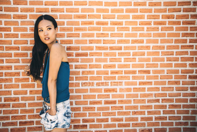 Довге волосся азіатська жінка позує на цегляній стіні — стокове фото