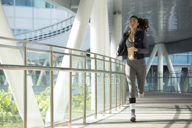 Eine junge asiatin joggt frühmorgens durch die stadt singapore. Sie passiert einen Abschnitt aus Stahl und Glas. — Stockfoto