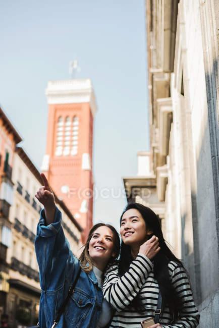 Two beautiful female friends walking in city and pointing — Stock Photo