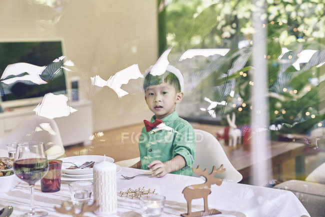 Pequeño asiático chico sentado en Navidad mesa y sonriendo - foto de stock