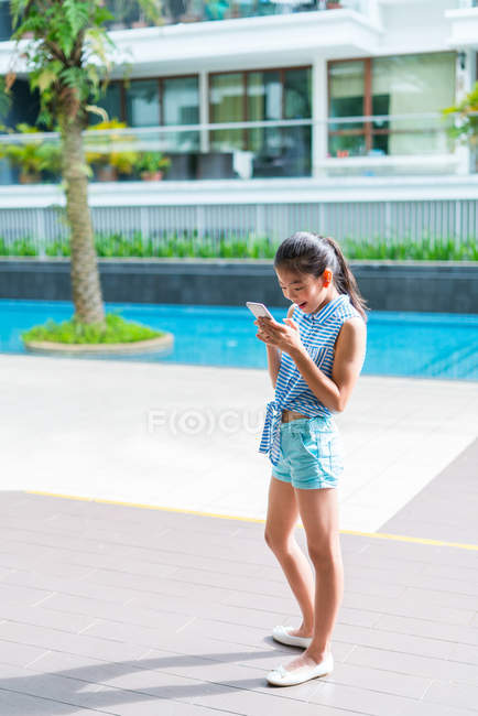 Jeune fille asiatique en utilisant smartphone à la piscine — Photo de stock