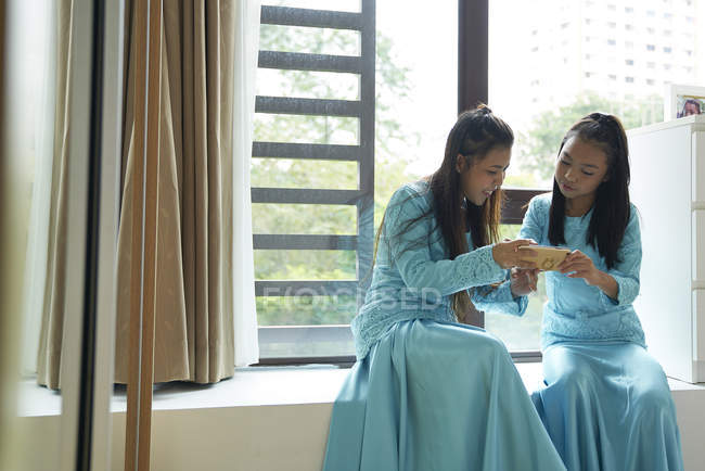 Due sorelle asiatiche guardando smartphone a casa — Foto stock