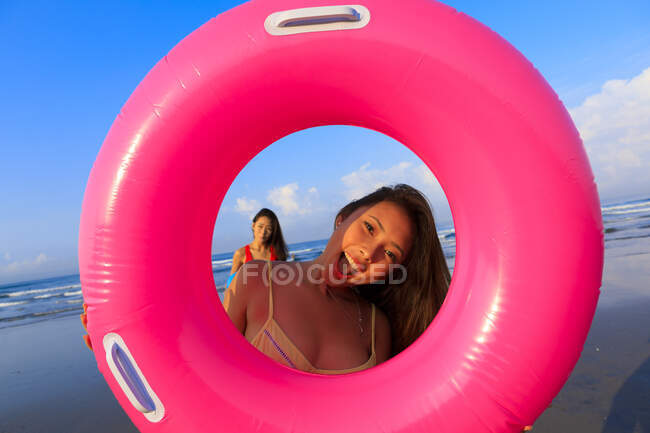 Dos jóvenes amigas asiáticas están jugando con sus flotadores en una playa en Bali. - foto de stock