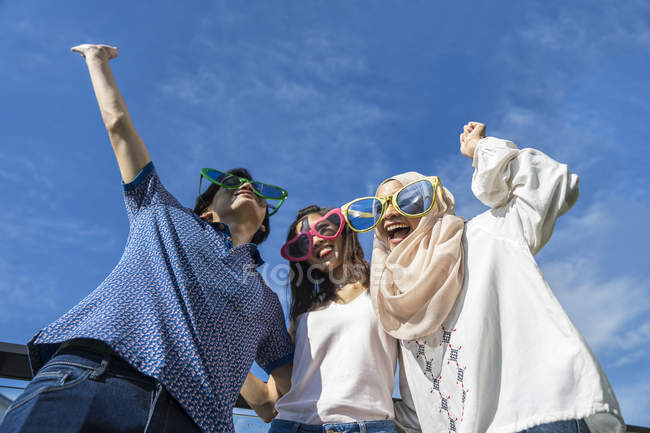 Groupe d'amis portant des lunettes drôles s'amusant contre le ciel bleu — Photo de stock