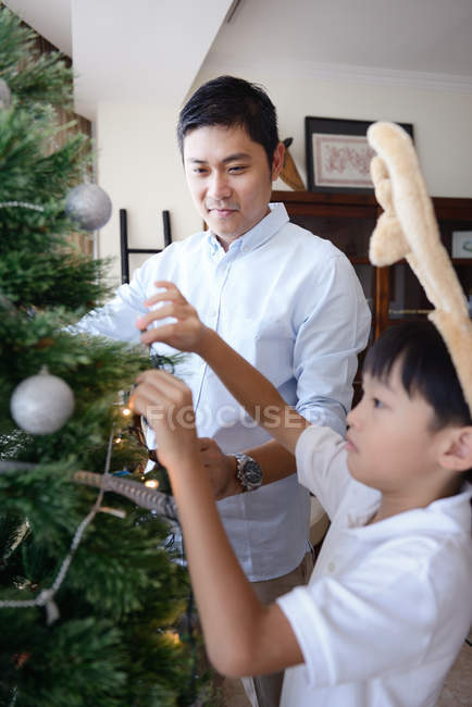 Happy young asian father and son decorating fir tree — Stock Photo