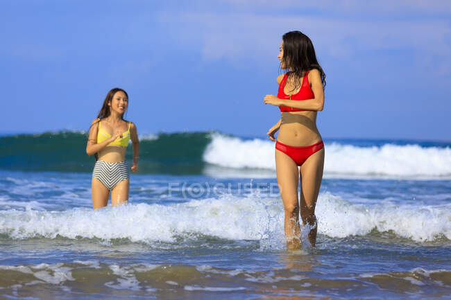 Dos jóvenes asiáticas se están divirtiendo en las olas del océano. - foto de stock