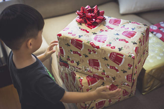 Un niño feliz y curioso abre sus regalos de Navidad - foto de stock