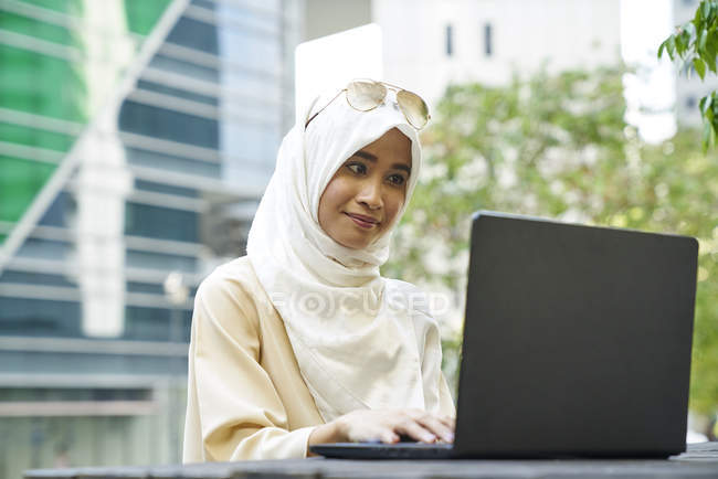 Allegro giovane donna in un Tudung digitando via sul suo computer portatile — Foto stock