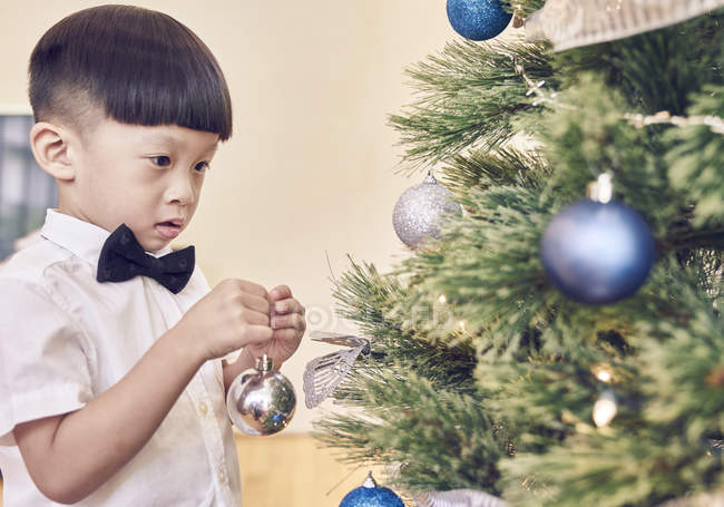 Happy young asian boy decorating christmas fir tree — Stock Photo