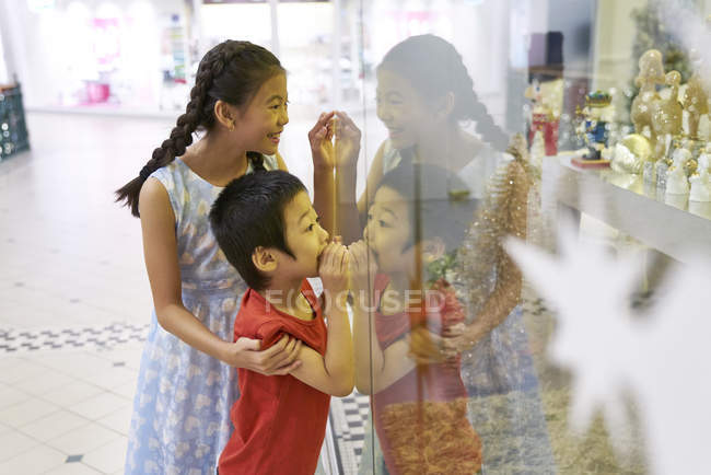 Little brother and sister looking through glass at mall — Stock Photo