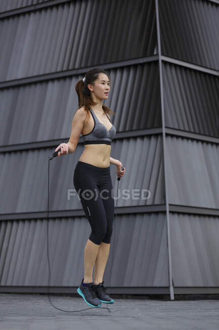 A young asian woman is exercising with rope jumping, outdoors in Singapore. — Stock Photo