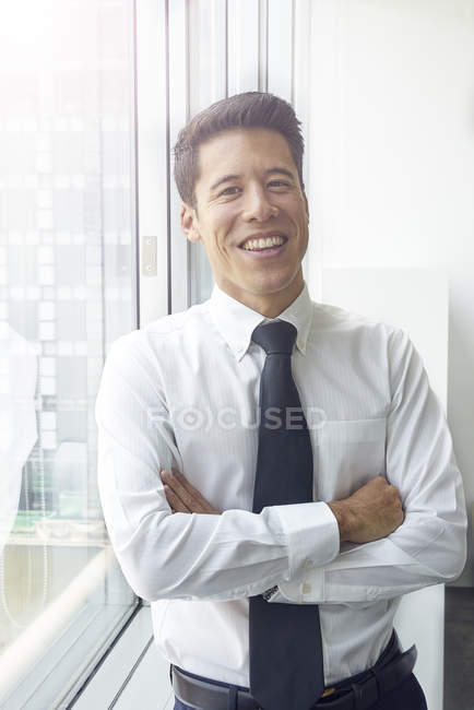 Guapo asiático hombre de negocios con corbata posando contra ventana - foto de stock