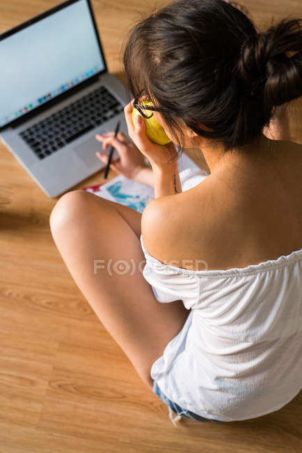 Joven mujer china comiendo manzana y trabajando con su computadora - foto de stock