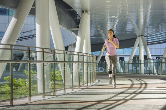 Une jeune femme asiatique fait du jogging dans la ville de Singapour tôt le matin. Elle passe une section d'architecture en acier et en verre . — Photo de stock