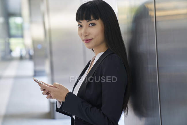 Молода приваблива азіатська бізнес-леді, використовуючи смартфон в сучасному офісі — стокове фото