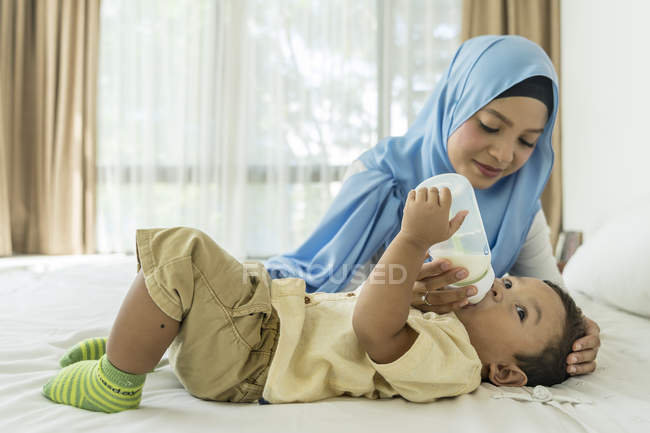 Joven asiático musulmán madre e hijo, madre alimentación bebé con leche biberón - foto de stock