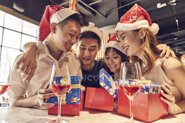 Счастливые молодые люди и их друзья вместе празднуют Новый год в кафе и делятся подарками — стоковое фото