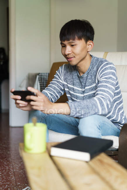 Дорослий азіатських юнак за допомогою смартфона в домашніх умовах — стокове фото