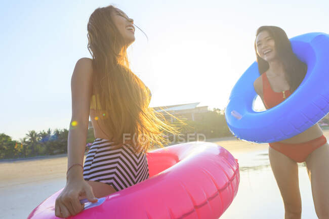 Zwei junge asiatische Freundinnen tummeln sich mit ihren Schwimmern an einem Strand auf Bali. — Stockfoto