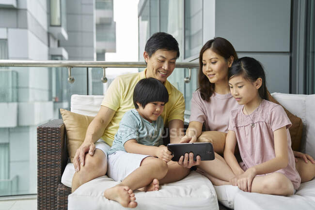 Счастливая молодая азиатская семья вместе с помощью цифрового планшета на дому — стоковое фото