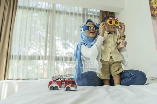 Joven asiático musulmán madre y niño tener divertido en casa con gafas de sol - foto de stock