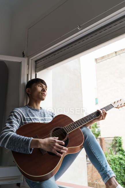 Young adult asian man playing on guitar at home — Stock Photo
