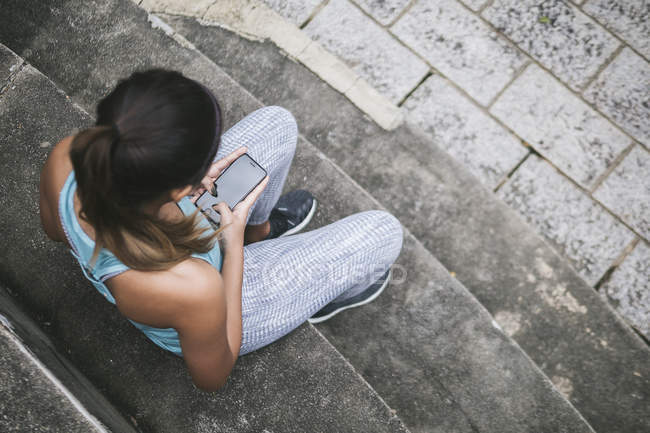 Молода азіатська спортивна жінка використовує смартфон на сходах — стокове фото