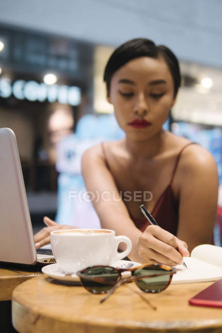 Jovem atraente asiático mulher escrevendo notas no café — Fotografia de Stock