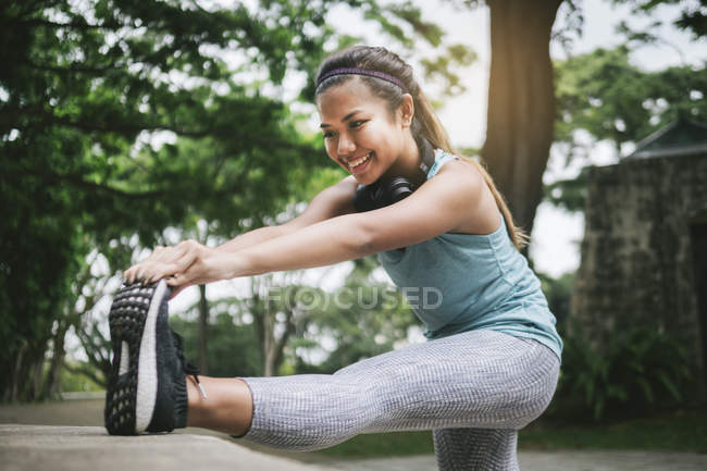 Joven asiático deportivo mujer haciendo estiramiento en parque - foto de stock