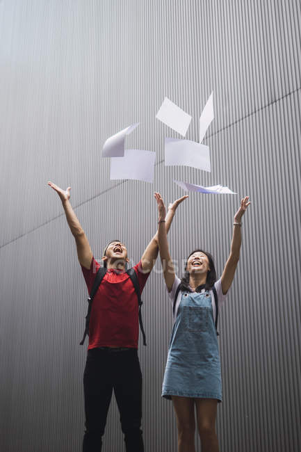 Молоді азіатські студенти коледжу кидають папір у повітря — стокове фото