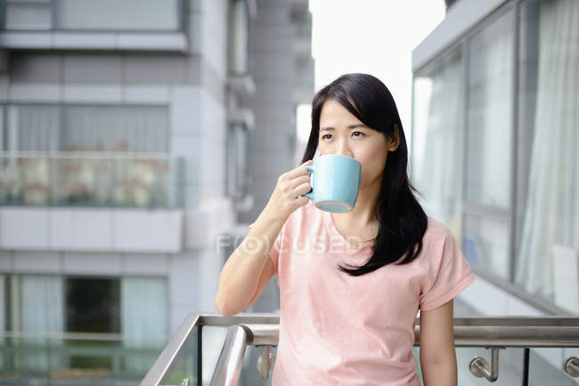 Young casual asian woman drinking tea on balcony — Stock Photo