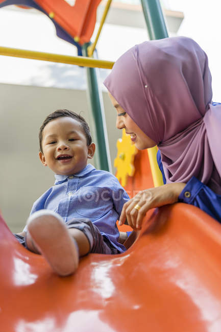 Joven asiático musulmán madre y niño jugando en parque infantil - foto de stock