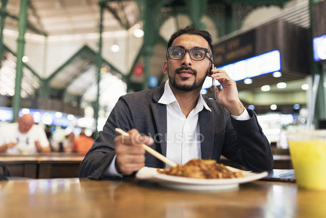 Красивый индийский бизнесмен, пользующийся смартфоном и питающийся в кафе — стоковое фото