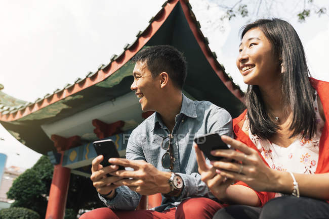 Joven feliz asiático pareja usando smartphones en chinatown - foto de stock
