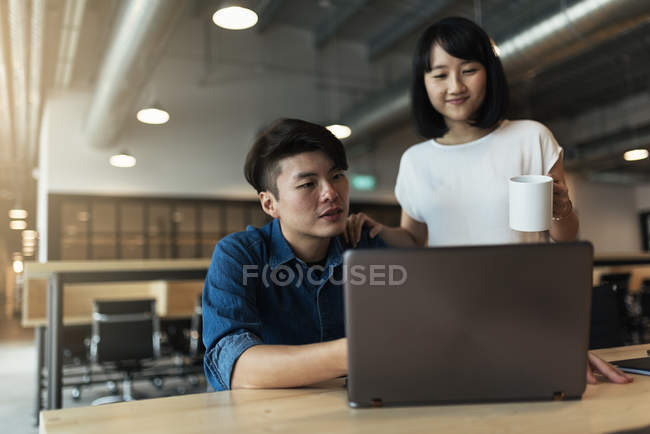 Two young asian people at work with laptop in modern office — Stock Photo