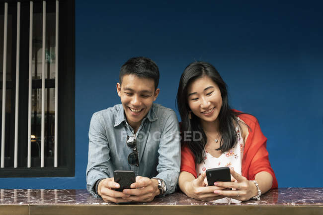 Young happy asian couple using smartphones — Stock Photo