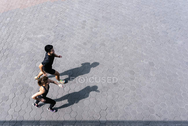 Young sporty couple running together on urban street — Stock Photo