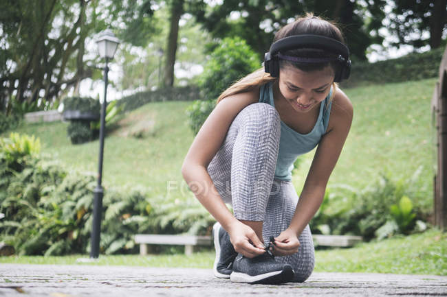 Молода азіатська спортивна жінка з навушниками, що зв'язують шнурки в парку — стокове фото