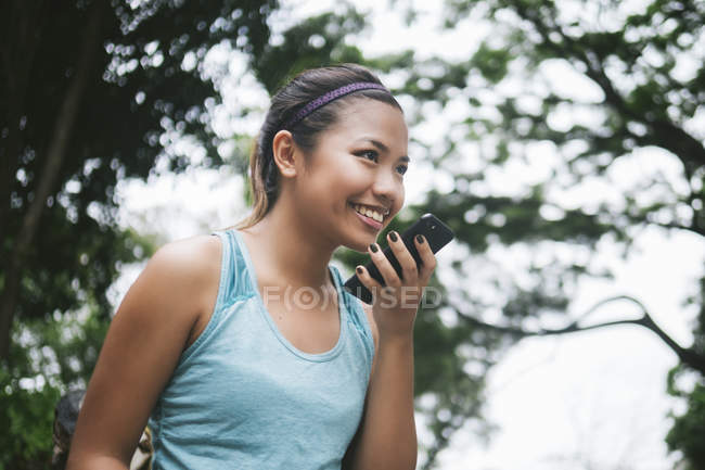 Молодая азиатская спортсменка с помощью смартфона в парке — стоковое фото