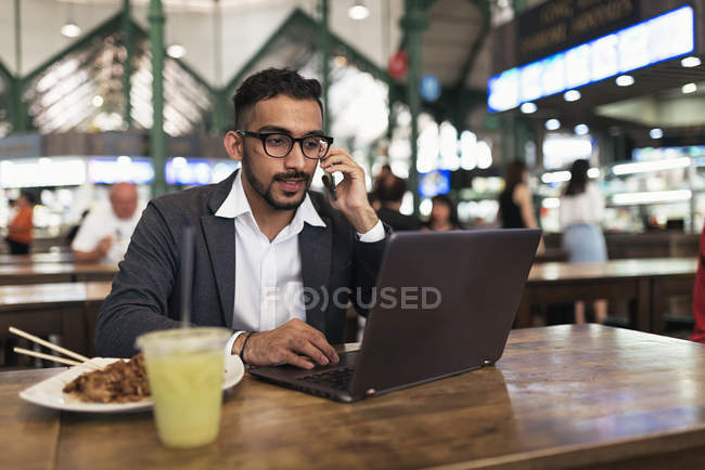 Красивий індійський бізнесмен використовує ноутбук і їсть в кафе — стокове фото
