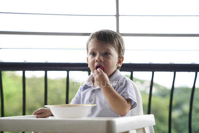 Baby boy eating in a baby seat on the balcony — Stock Photo